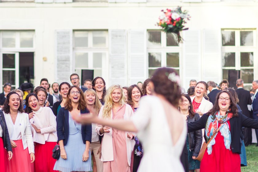 Le bouquet de la mariée en suspension au-dessus des invitées réunies devant le château, éclats de rire et bras tendus