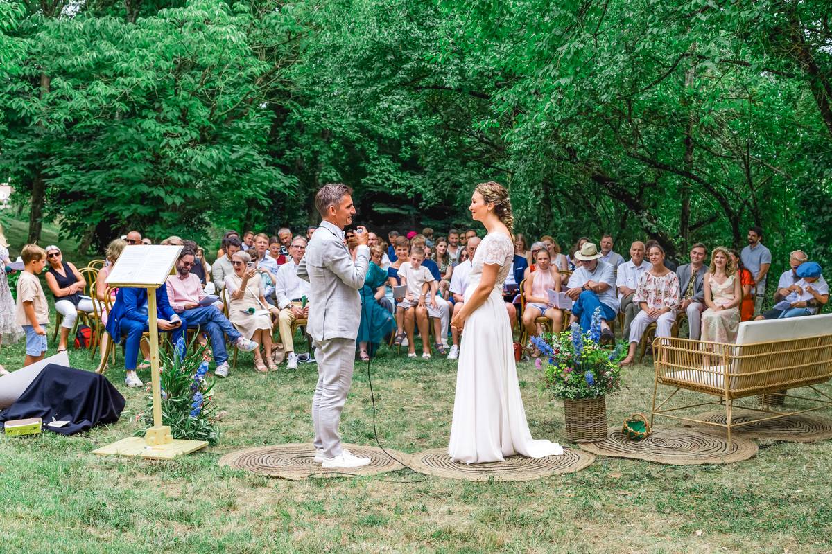 Cérémonie laïque en plein air sous les arbres, mariée face à l'officiant devant les invités