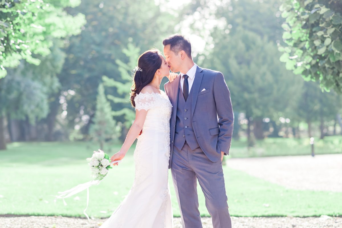 Couple de mariés s'embrassant dans un parc arboré, lumière naturelle douce, reportage mariage