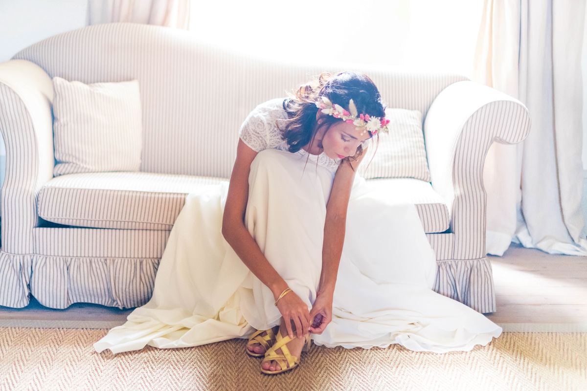 Mariée en couronne de fleurs ajustant ses sandales pendant les préparatifs, lumière naturelle