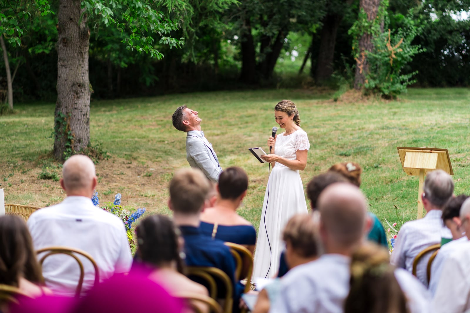 Cérémonie laïque en plein air sous les grands arbres, la mariée prend la parole au micro face aux invités assis