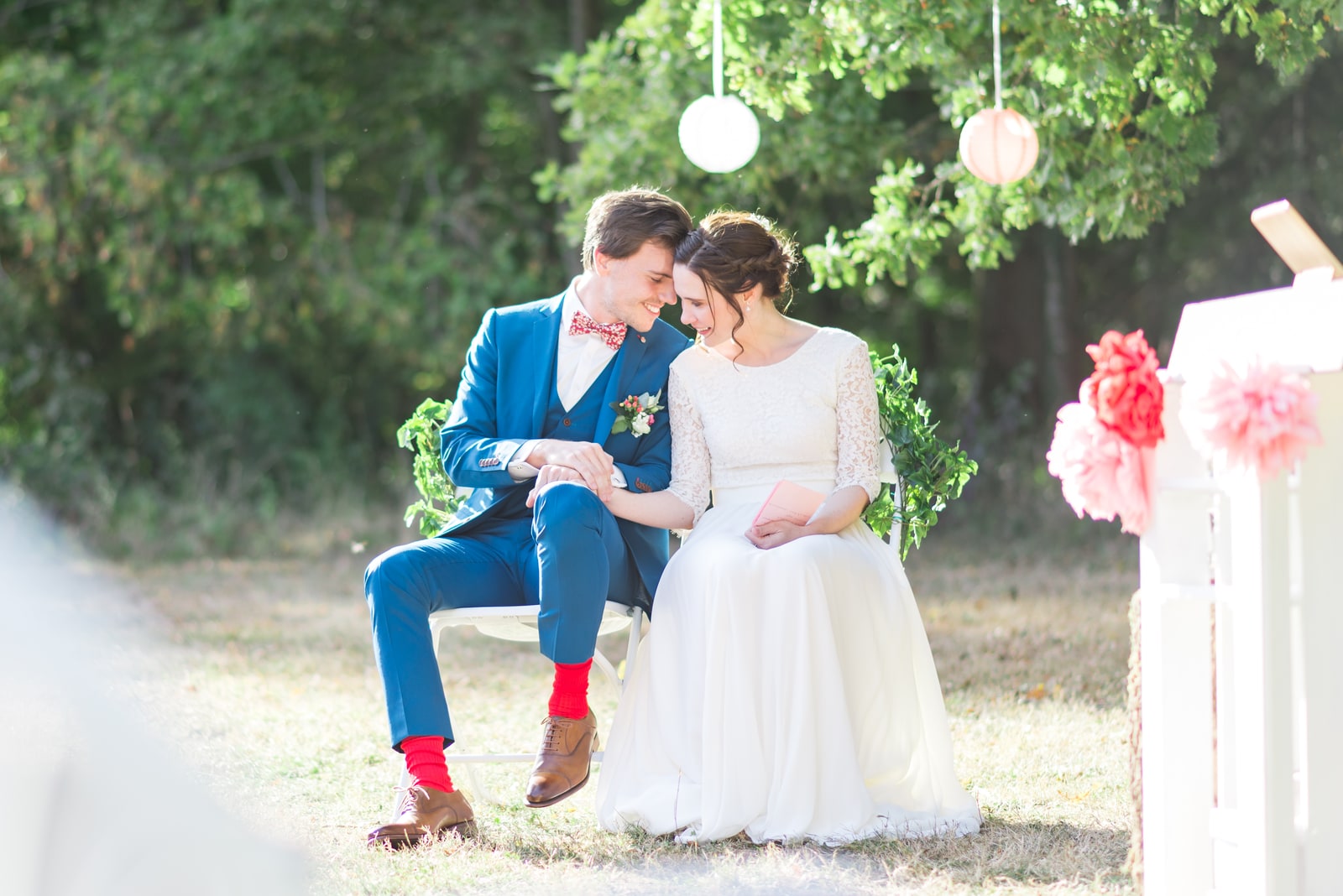 Les mariés assis pendant la cérémonie, costume bleu et chaussettes rouges, sous des pompons de papier suspendus