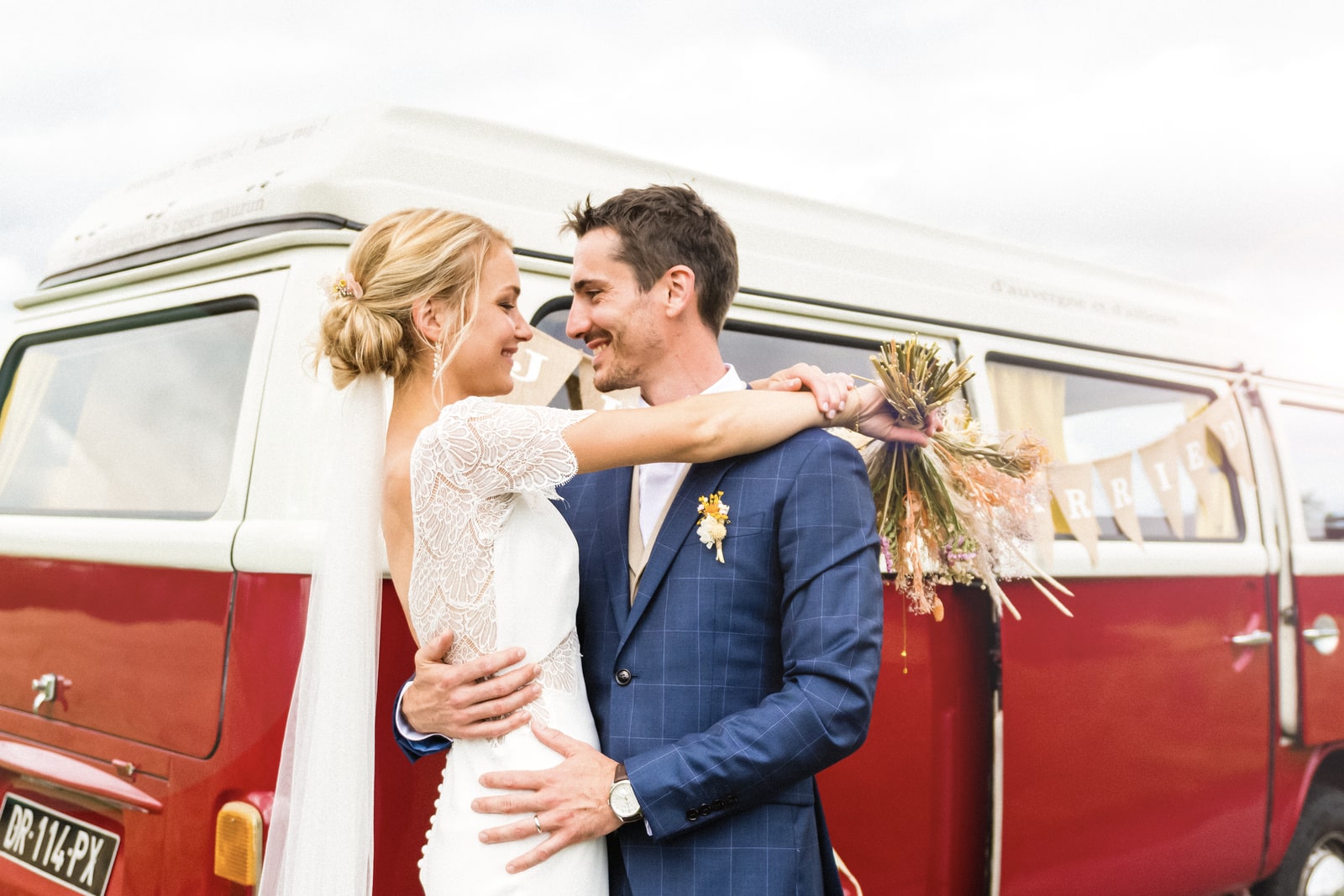 Les mariés posent devant un combi Volkswagen rouge et blanc décoré pour le mariage