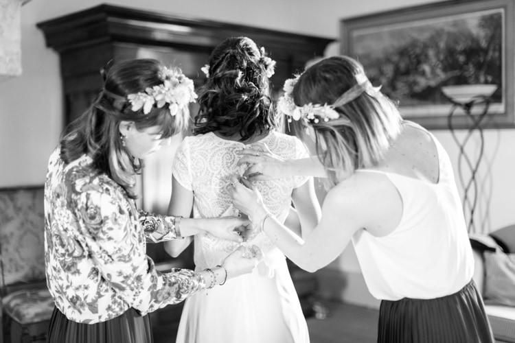 Trois demoiselles d'honneur lacent le dos de la robe de la mariée, couronnes de fleurs dans les cheveux