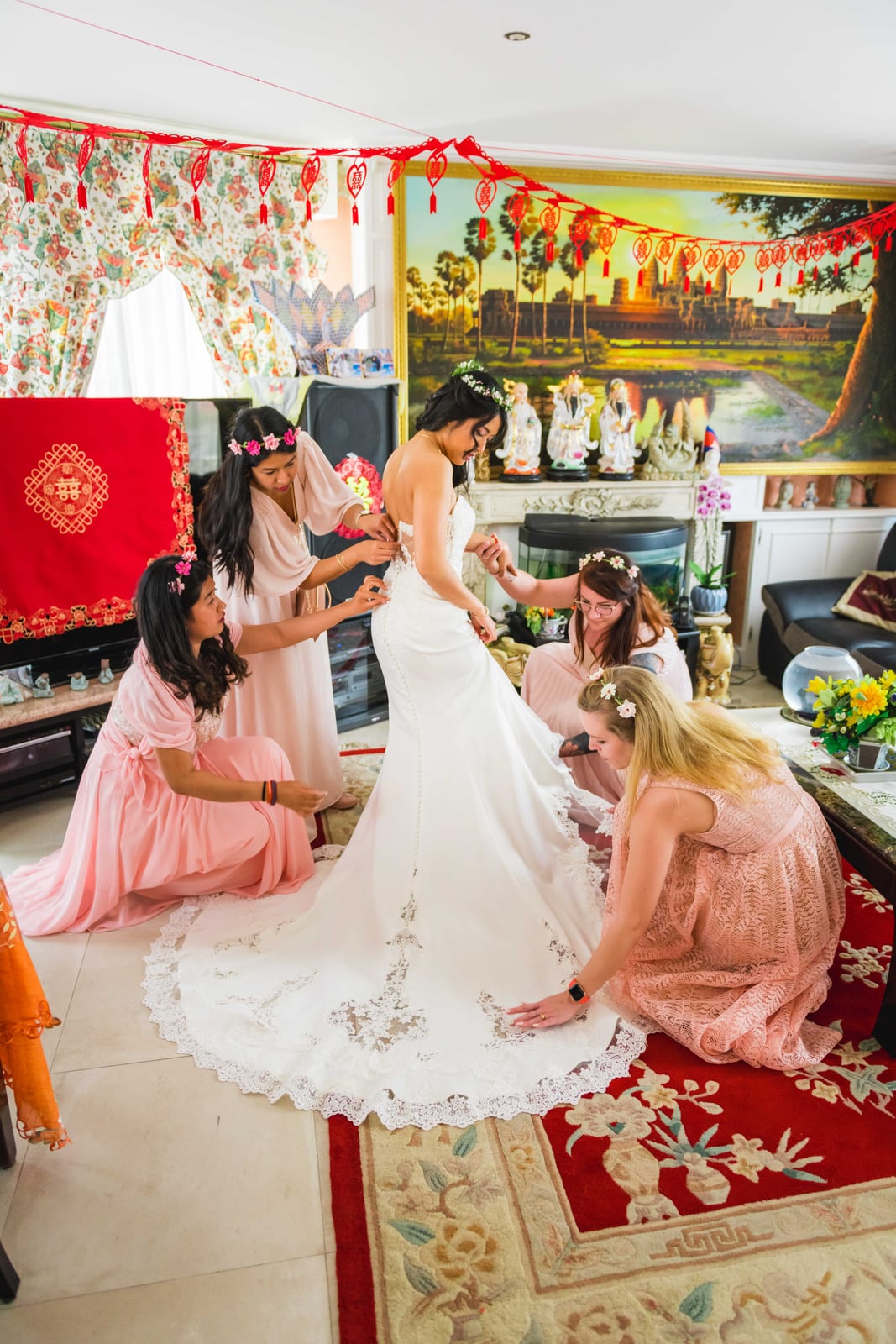 La mariée entourée de ses demoiselles d'honneur en rose qui ajustent sa traîne, dans un intérieur décoré de rouge