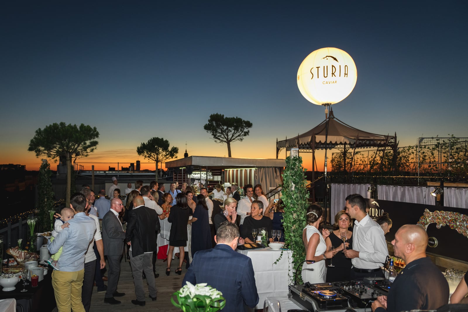 Soirée en terrasse au crépuscule, un ballon lumineux suspendu au-dessus du buffet et des invités
