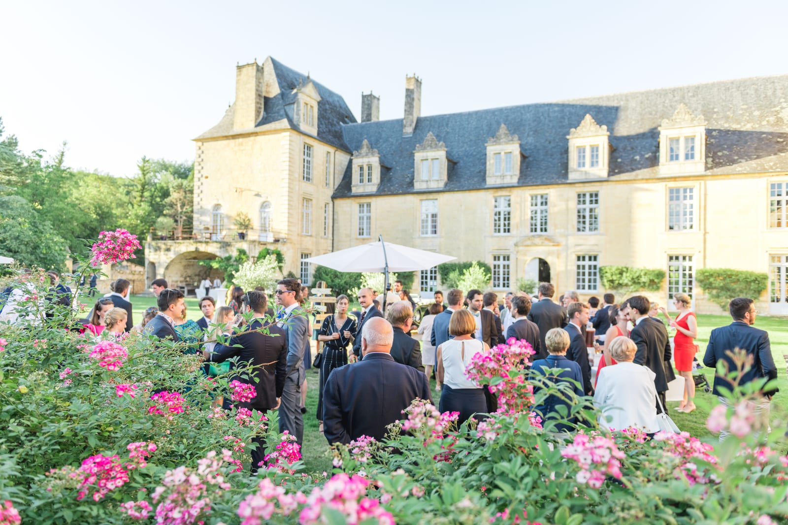 Les invités réunis dans un jardin de roses au pied d'un château à toit d'ardoise